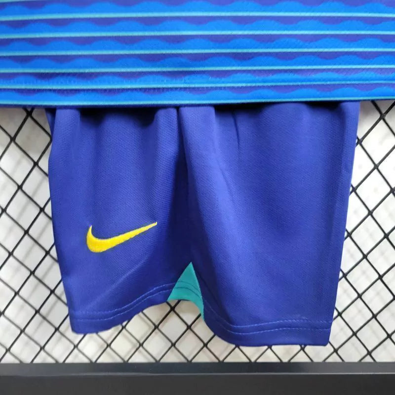 "Kit Infantil Brasil Away 2024/25 Nike, camisa azul com detalhes em verde e amarelo, shorts e meias combinando, uniforme oficial da Seleção Brasileira para torcedores mirins."