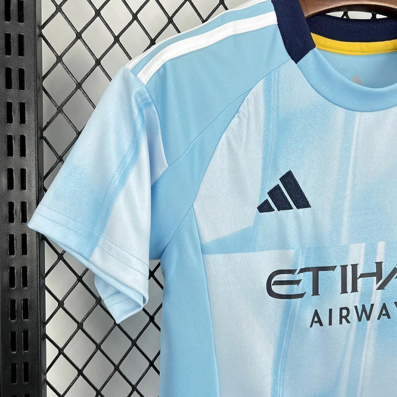 Kit Infantil New York City Home 2025/26 Adidas – Camisa azul clara com detalhes geométricos inspirados nos prédios de Nova York, calção azul marinho e meias combinando, modelo infantil