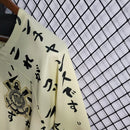 Camisa do Corinthians com estampa japonesa em katakana, escudo bordado no peito, modelo unissex em tom bege, pendurada em cabide sobre fundo de grade metálica. Design exclusivo estilo retrô edição limitada 2024.