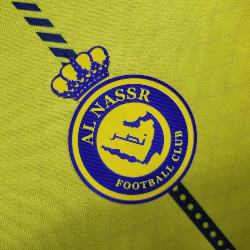 Camisa Al-Nassr Home (1) 2023/24 Nike Torcedor Masculina amarela com detalhes azuis, escudo do Al-Nassr e logo Nike bordados, modelo oficial usado por Cristiano Ronaldo."
