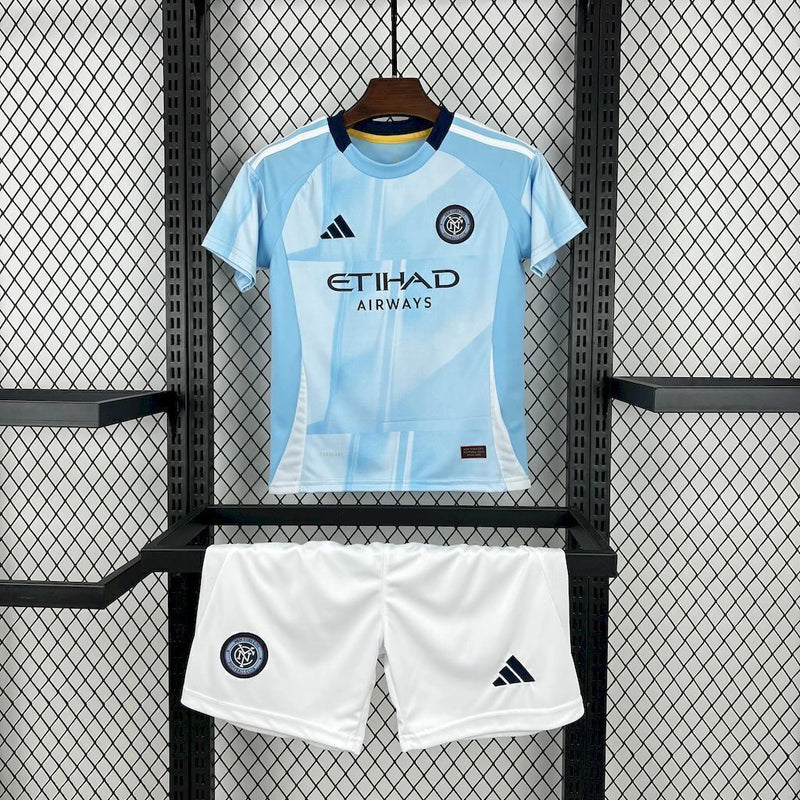Kit Infantil New York City Home 2025/26 Adidas – Camisa azul clara com detalhes geométricos inspirados nos prédios de Nova York, calção azul marinho e meias combinando, modelo infantil