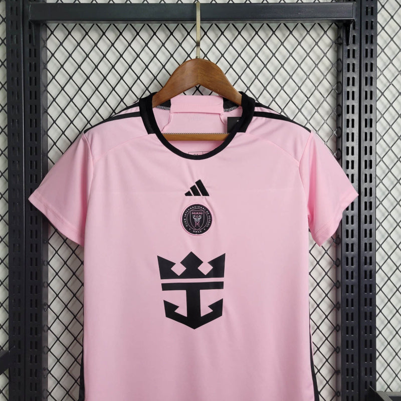 "Kit Infantil Inter Miami Home (1) 2024/25 Adidas oficial, camisa branca com detalhes em rosa e preto, escudo do Inter Miami CF em destaque, shorts e meias combinando, uniforme completo para crianças de 3 a 13 anos"