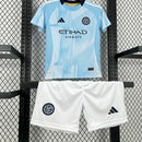 Kit Infantil New York City Home 2025/26 Adidas – Camisa azul clara com detalhes geométricos inspirados nos prédios de Nova York, calção azul marinho e meias combinando, modelo infantil