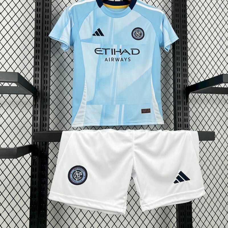 Kit Infantil New York City Home 2025/26 Adidas – Camisa azul clara com detalhes geométricos inspirados nos prédios de Nova York, calção azul marinho e meias combinando, modelo infantil