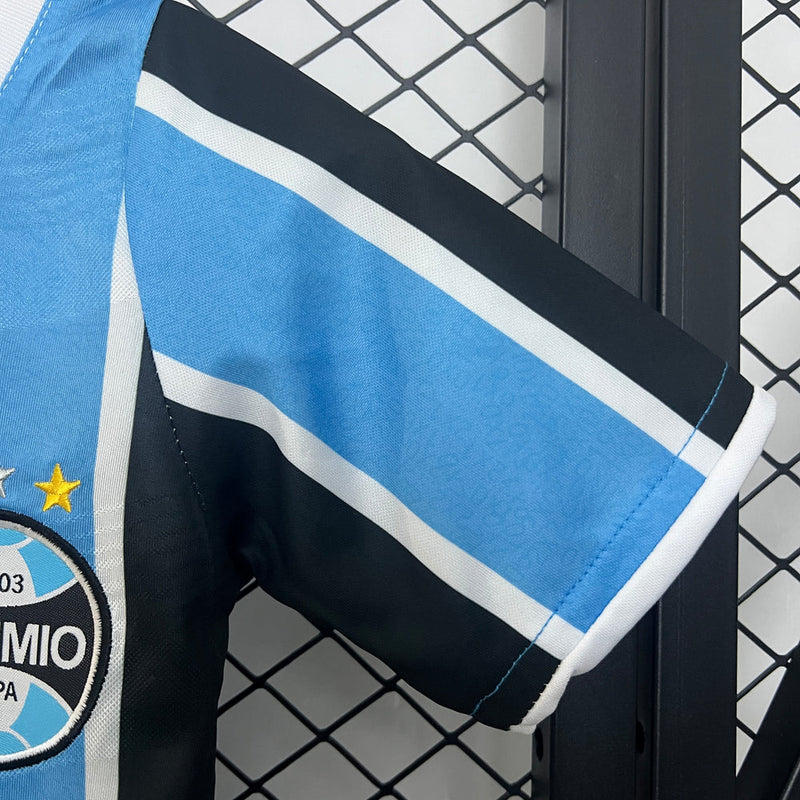 "Kit Infantil Grêmio Home 2024/25 Umbro, camisa azul, preta e branca listrada com shorts e meias combinando, uniforme oficial para crianças de 3 a 13 anos torcedoras do Grêmio."