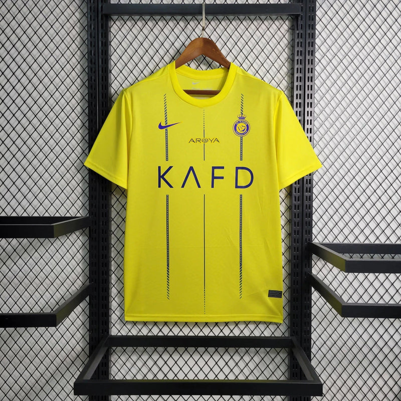 Camisa Al-Nassr Home (1) 2023/24 Nike Torcedor Masculina amarela com detalhes azuis, escudo do Al-Nassr e logo Nike bordados, modelo oficial usado por Cristiano Ronaldo."
