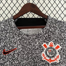 Camisa Corinthians 2023/24 Edição Especial Nike Torcedor Masculina com estampa preta e branca estilo caderno universitário, escudo bordado e logo Nike vermelho, pendurada em cabide contra uma grade metálica.