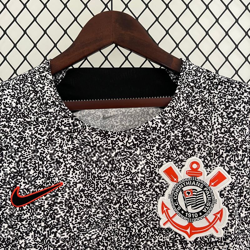 Camisa Corinthians 2023/24 Edição Especial Nike Torcedor Masculina com estampa preta e branca estilo caderno universitário, escudo bordado e logo Nike vermelho, pendurada em cabide contra uma grade metálica.