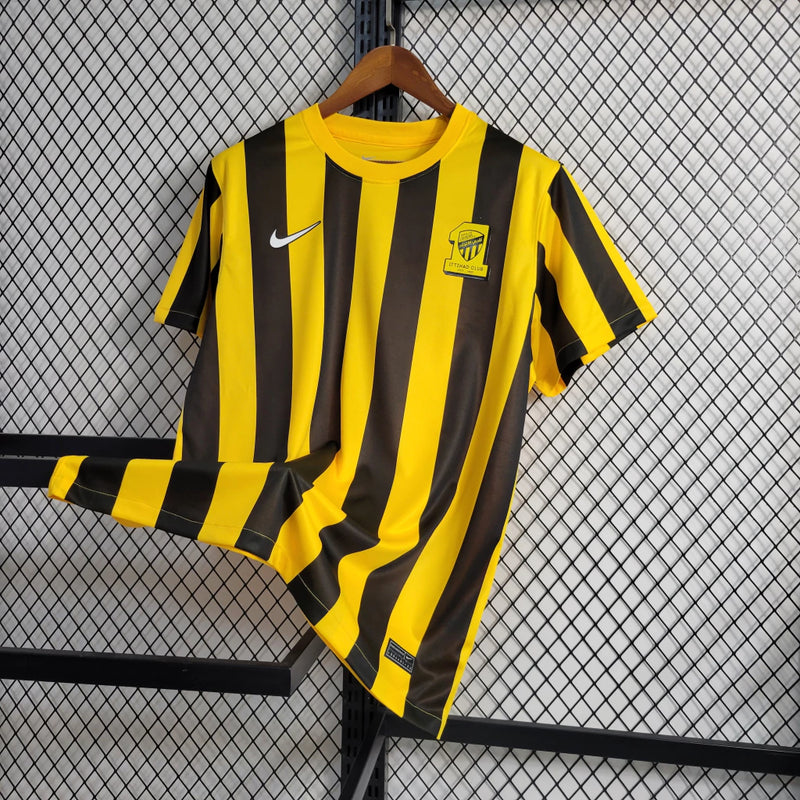 Camisa Al-Ittihad Home I 2023/24 Nike Torcedor Masculina amarela com detalhes em preto, uniforme titular do Al-Ittihad Club da Arábia Saudita, modelo torcedor com tecido leve e tecnologia Dri-FIT para absorção de suor."