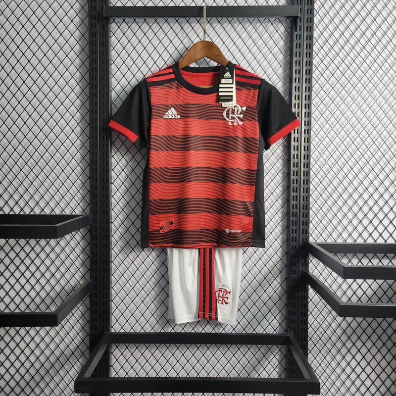 Kit Infantil Flamengo Home 2022/23 Adidas, camisa vermelha e preta com listras horizontais, shorts e meias combinando, uniforme oficial para torcedores mirins do Mengão, idades de 3-4 a 12-13 anos."