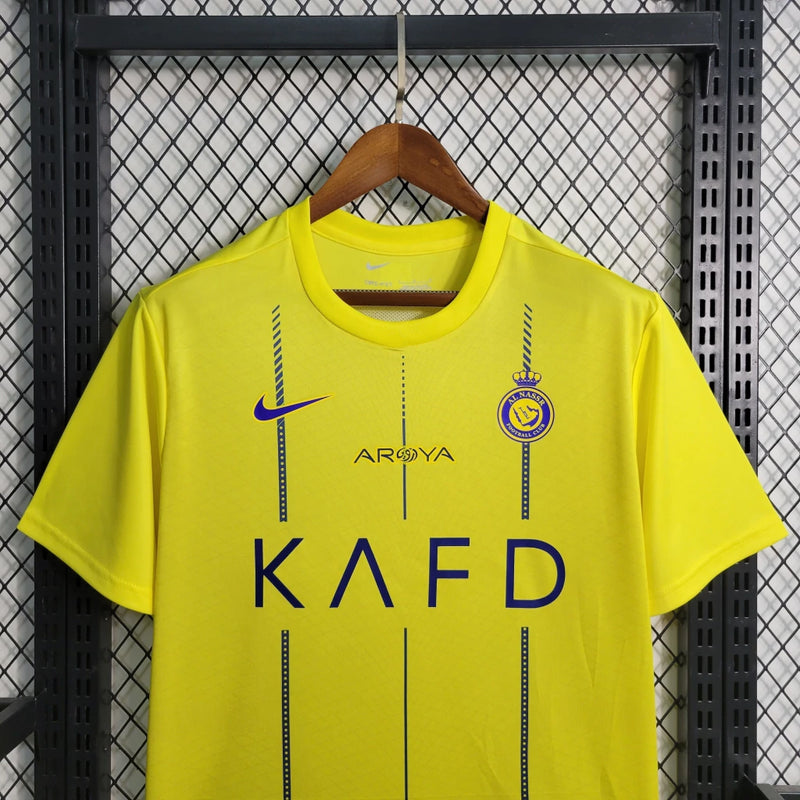 Camisa Al-Nassr Home (1) 2023/24 Nike Torcedor Masculina amarela com detalhes azuis, escudo do Al-Nassr e logo Nike bordados, modelo oficial usado por Cristiano Ronaldo."

