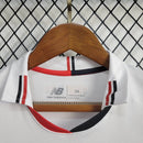 Kit Infantil São Paulo Home (1) 2024/25 New Balance oficial – camisa branca com listras vermelha, preta e branca, short e meião. Uniforme infantil do São Paulo FC temporada 2024/2025."