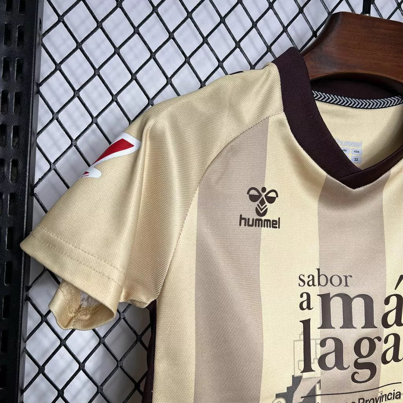 Kit Infantil Málaga CF Third III 2024/25 Hummel com camisa e short dourados, uniforme infantil leve e respirável, ideal para jogos, treinos e jovens torcedores do Málaga CF."