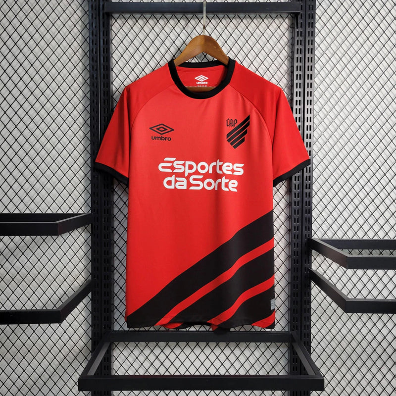 Camisa Athletico Paranaense Home (1) 2023/24 Umbro Torcedor Masculina com escudo oficial bordado e logo Umbro estampado, modelo clássico vermelho e preto do clube paranaense.