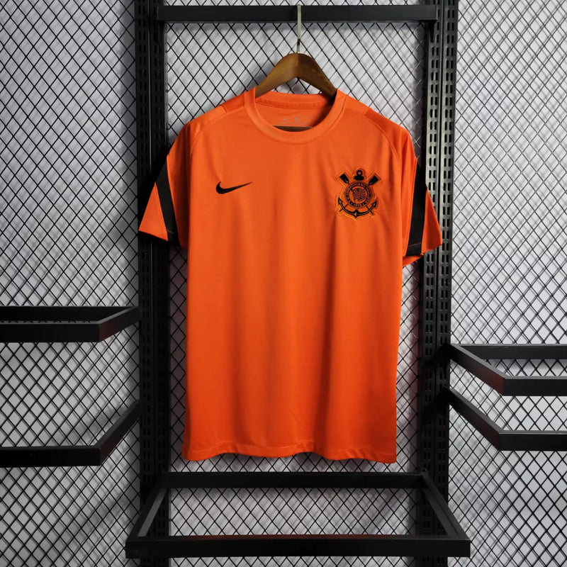 Vista frontal da Camisa Corinthians Treino 2022/23 Nike Laranja, com escudo do clube e logo Nike em destaque"