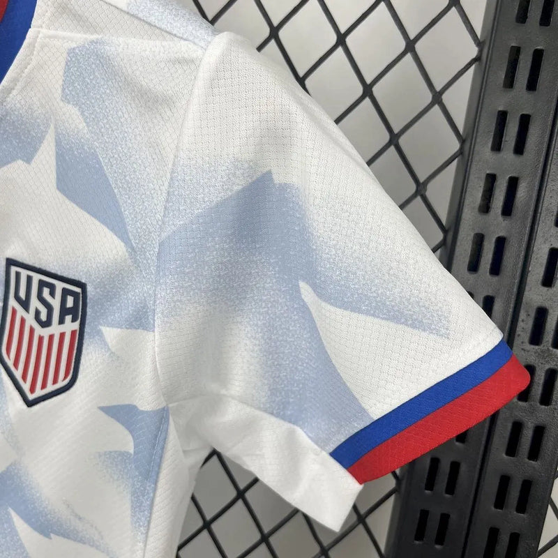 Kit Infantil Estados Unidos Home (1) 2025/26 Nike, uniforme oficial branco com detalhes em azul e vermelho, composto por camisa e shorts, disponível dos 3-4 aos 12-13 anos."