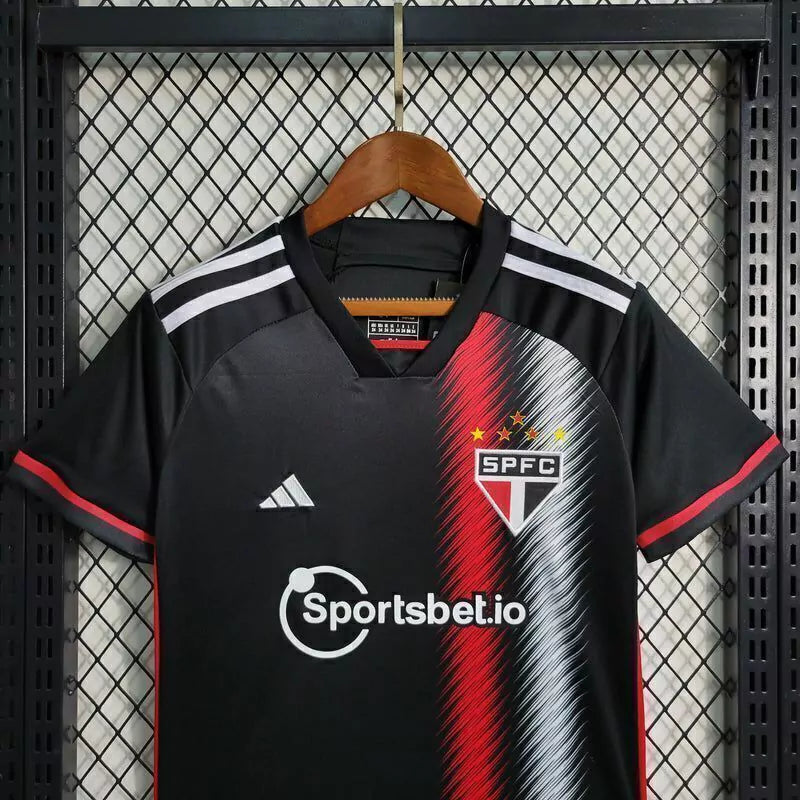 Kit Infantil São Paulo Away III 2023/24 Adidas, camisa preta com detalhes em vermelho e branco, shorts e meias combinando, uniforme oficial para torcedores mirins do São Paulo FC