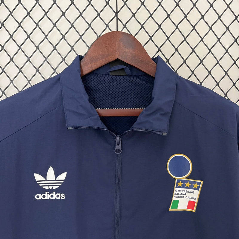 Corta-Vento Itália 2024/25 Adidas Masculino, azul, com escudo da seleção italiana e logo Adidas em destaque, tecido leve, respirável e resistente ao vento, com bolsos laterais e ajuste confortável, ideal para uso casual ou esportivo.”