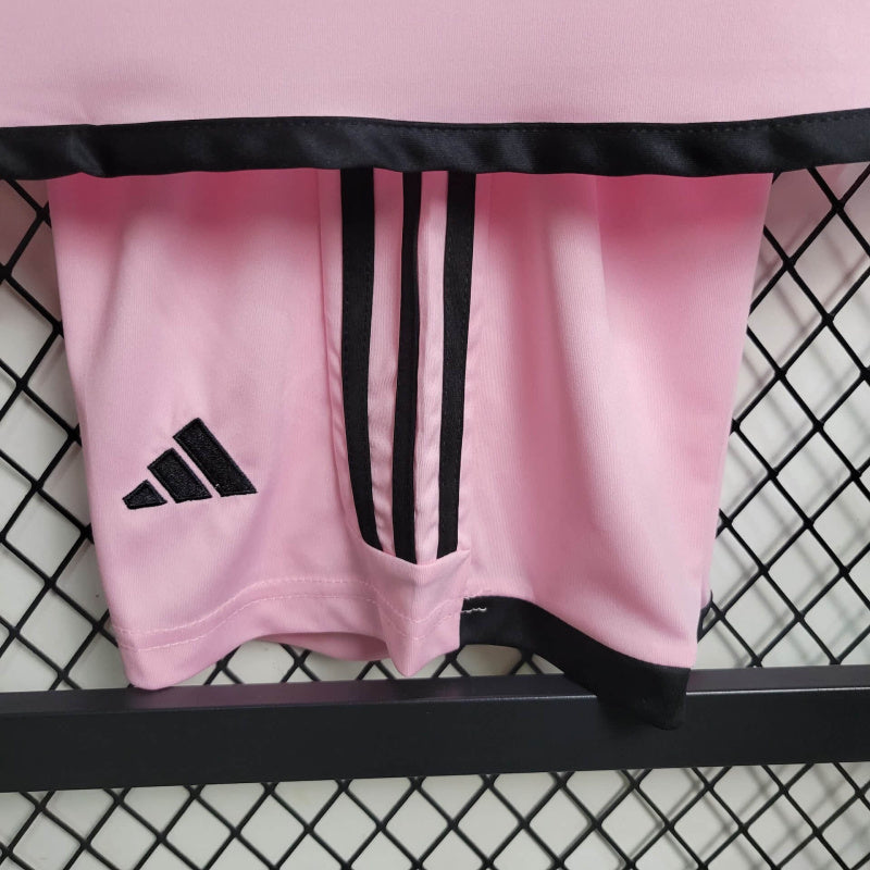 "Kit Infantil Inter Miami Home (1) 2024/25 Adidas oficial, camisa branca com detalhes em rosa e preto, escudo do Inter Miami CF em destaque, shorts e meias combinando, uniforme completo para crianças de 3 a 13 anos"