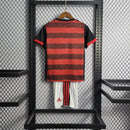 Kit Infantil Flamengo Home 2022/23 Adidas, camisa vermelha e preta com listras horizontais, shorts e meias combinando, uniforme oficial para torcedores mirins do Mengão, idades de 3-4 a 12-13 anos."