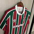
Camisa Fluminense Home 2025/26 Umbro Torcedor Masculina tricolor com listras verticais em verde, grená e branco, escudo bordado no peito e design moderno da temporada 2025/26