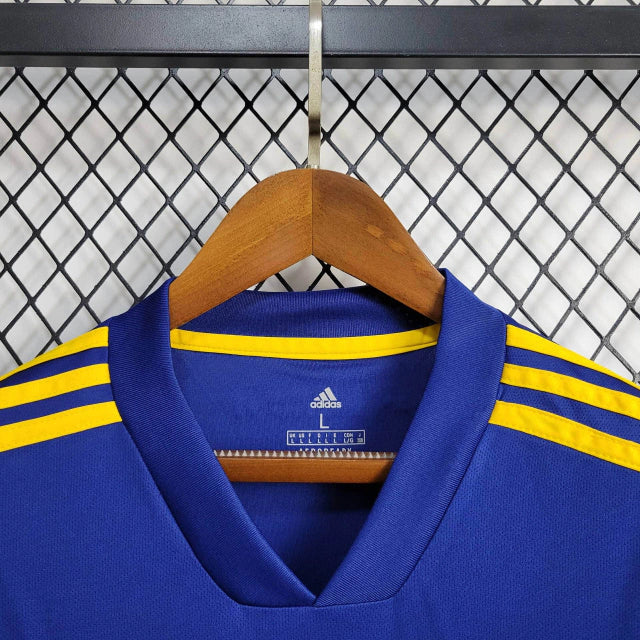 Texto alternativo para imagem:
Camisa Boca Juniors Home (1) 2020/21 Retrô Adidas Masculina azul com faixa amarela, escudo bordado e logo Adidas clássico estampado.

