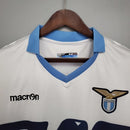 Camisa Lazio Home I 2014/15 Retrô Masculina branca com detalhes em azul celeste, gola em “V” azul e escudo bordado, representando a elegância e tradição do futebol italiano e da torcida Biancoceleste.