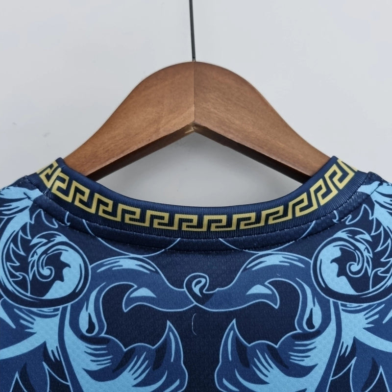 Camisa Concept Itália x Versace Puma Torcedor masculina, azul, com escudo da seleção italiana no peito, detalhes exclusivos da Versace e três listras Puma nos ombros, feita em tecido leve e respirável, modelo com caimento confortável, ideal para torcer com estilo e exclusividade.”