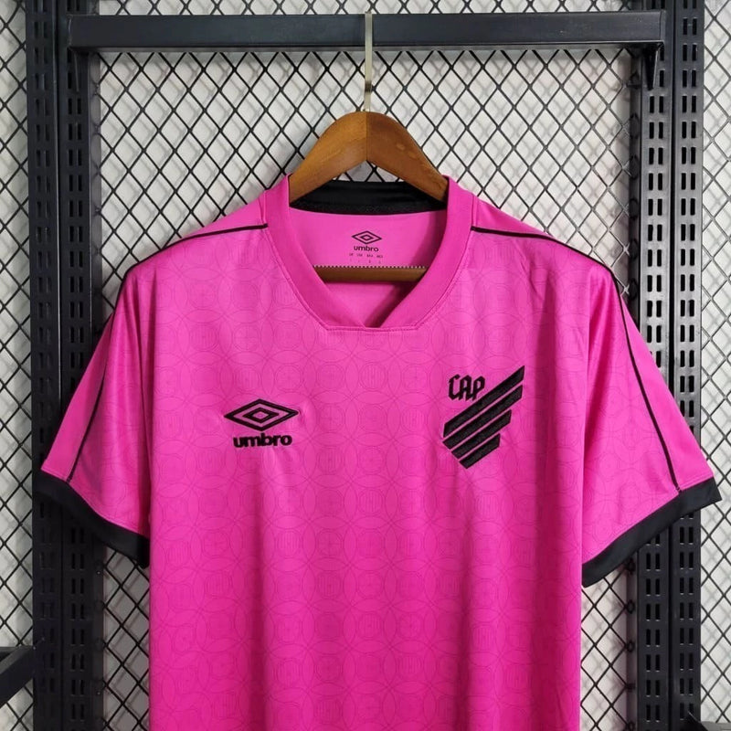 Camisa Athletico Paranaense Outubro Rosa 2023/24 Umbro Torcedor Masculina rosa vibrante com escudo oficial bordado e logo Umbro estampado, edição especial de conscientização contra o câncer de mama.
