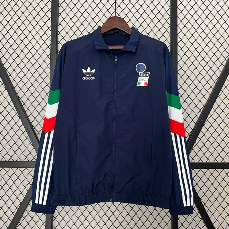 Corta-Vento Itália 2024/25 Adidas Masculino, azul, com escudo da seleção italiana e logo Adidas em destaque, tecido leve, respirável e resistente ao vento, com bolsos laterais e ajuste confortável, ideal para uso casual ou esportivo.”